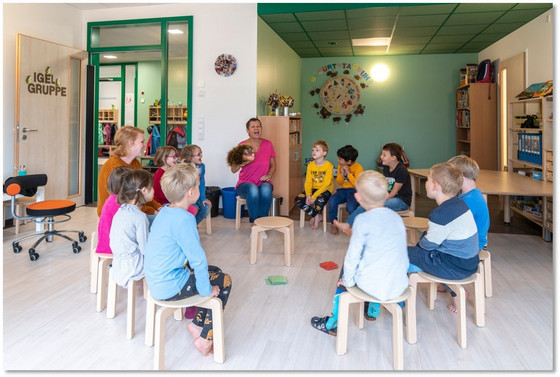 Zahlreiche Kindergartenkinder der Igel-Gruppe sitzen mit zwei Betreuerinnen in einem Stuhlkreis und blicken auf eine Igel-Handpuppe einer Betreuerin in der Albertinen Kindertagesstätte Schnelsen in Hamburg.
