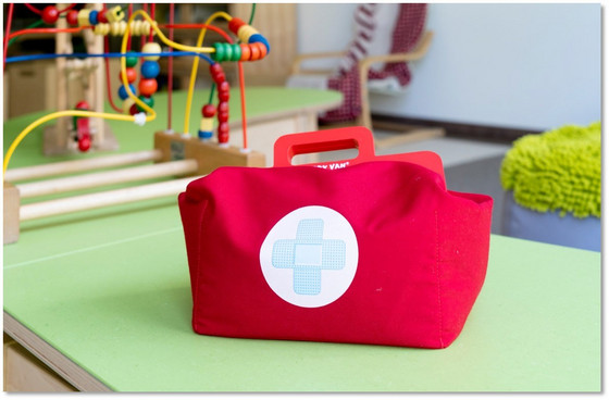 Eine rote Tasche mit einem aufgedruckten Erste-Hilfe-Kreuz steht auf einem Boden mit Spielzeug und bunten Teppichen in der Albertinen Kindertagesstätte Schnelsen in Hamburg.