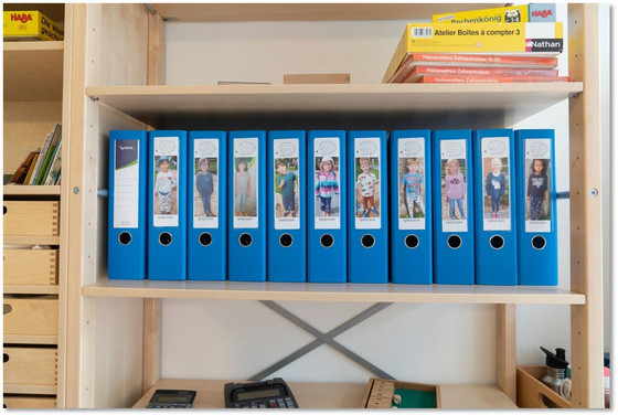 Mehrere blaue Aktenordner mit Kinderfotos auf dem Ordnerrücken in einem Regal in der Albertinen Kindertagesstätte Schnelsen in Hamburg.