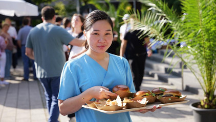 Eine Pflegekraft in blauer Funktionskleidung trägt ein Tablett mit Burger und Pommes beim Albertinen-Sommerfest für die Mitarbeitenden aus den unterschiedlichen Einrichtungen der Immanuel Albertinen Diakonie am Standort Schnelsen auf dem Platz vor der Kirche am Albertinen Krankenhaus. Eine Pflegekraft in blauer Funktionskleidung trägt ein Tablett mit Burger und Pommes beim Albertinen-Sommerfest für die Mitarbeitenden aus den unterschiedlichen Einrichtungen der Immanuel Albertinen Diakonie am Standort Schnelsen auf dem Platz vor der Kirche am Albertinen Krankenhaus.